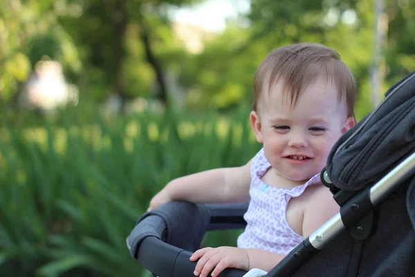 Weinig, mooi, glimlachend, schattige roodharige baby in een kinderwagen out-of-Doors in een mouwloos shirt op zoek naar beneden — Stockfoto