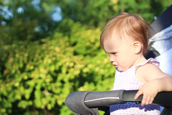 Weinig, mooi, glimlachend, schattige roodharige baby in een kinderwagen out-of-Doors in een mouwloos shirt op zoek naar beneden — Stockfoto