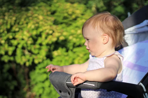 Pequeño, hermoso, sonriente, lindo bebé pelirrojo en un cochecito al aire libre en una camisa sin mangas mirando hacia el futuro —  Fotos de Stock