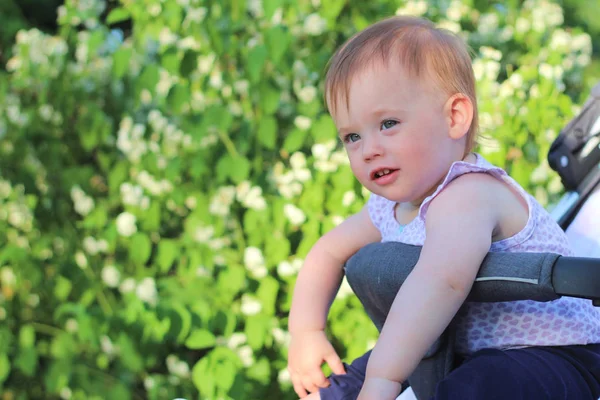 Pequeño, hermoso, sonriente, lindo bebé pelirrojo en una camisa sin mangas en un cochecito al aire libre cae las manos hacia abajo y mirando hacia adelante —  Fotos de Stock