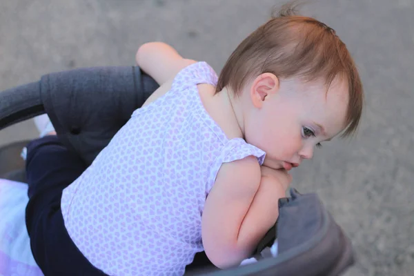 Weinig, mooie, glimlachend, schattige roodharige baby in een mouwloos overhemd in een kinderwagen out-of-Doors DROPS hands-down en terugkijkend — Stockfoto