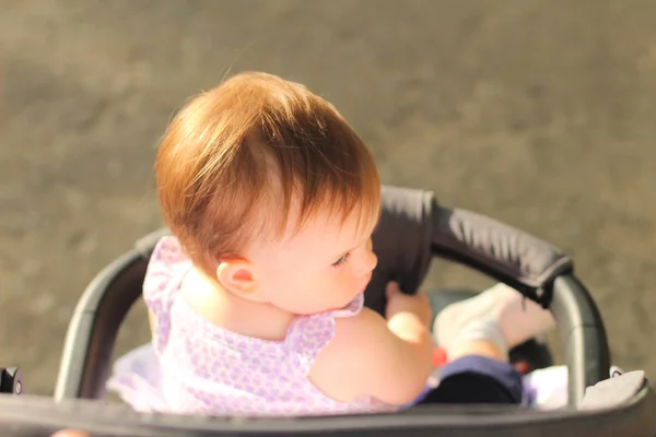 Weinig, mooie, glimlachend, schattige roodharige baby in een mouwloos overhemd in een kinderwagen out-of-Doors DROPS hands-down en terugkijkend — Stockfoto