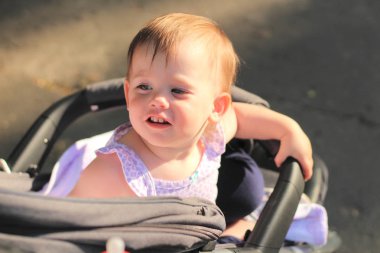 küçük, güzel, gülümseyen, sevimli kızıl saçlı bebek kolsuz gömlek bir bebek arabası içinde-of-doors ellerini aşağı düşer ve geriye bakarak