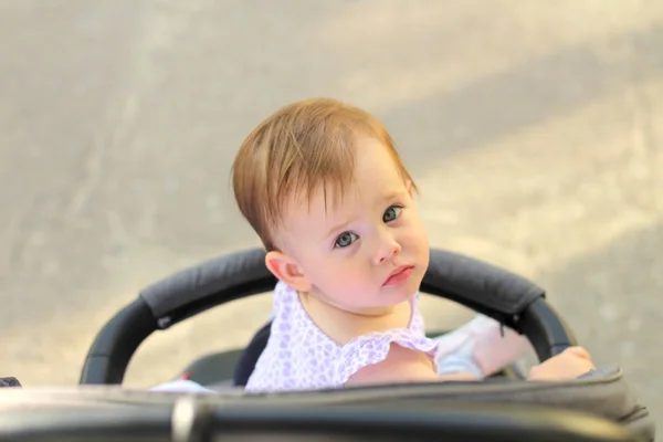 Kleines, schönes, lächelndes, niedliches rothaariges Baby in ärmellosem Hemd im Kinderwagen vor der Tür fällt die Hände nach unten und blickt zurück — Stockfoto