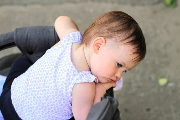 Pequeno, lindo, sorrindo, bebê ruiva bonito em uma camisa sem mangas em um carrinho fora de portas cai as mãos para baixo e olhando para trás — Fotografia de Stock