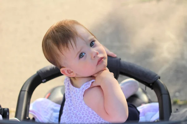 Weinig, mooie, glimlachend, schattige roodharige baby in een mouwloos overhemd in een kinderwagen out-of-Doors DROPS hands-down en terugkijkend — Stockfoto