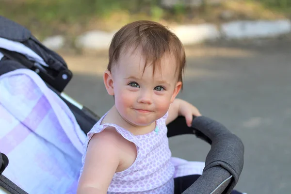 Weinig, mooi, glimlachend, schattige roodharige baby in een mouwloos overhemd in een kinderwagen out-of-Doors DROPS hands-down en Vooruitkijkend — Stockfoto