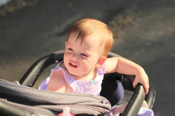 Pequeño, hermoso, sonriente, lindo bebé pelirrojo en una camisa sin mangas en un cochecito al aire libre cae las manos hacia abajo y mirando hacia atrás —  Fotos de Stock