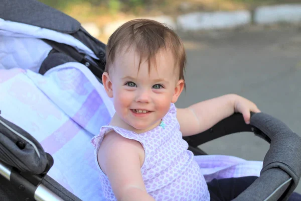 Weinig, mooi, glimlachend, schattige roodharige baby in een mouwloos overhemd in een kinderwagen out-of-Doors DROPS hands-down en Vooruitkijkend — Stockfoto