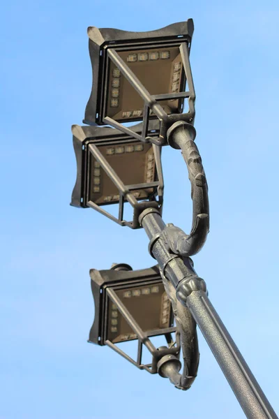 Photo of three modern metal LED lamps in vintage style on a single post against a blue sky — Stock Photo, Image