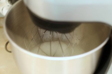 Bir restoranda profesyonel mutfak karıştırıcı yumurta akı kırbaçlama. Yakın çekim çırpılmış beyazlar ve şeker bir metal gezegen karıştırıcı kase.