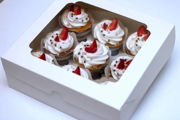 Cupcakes de primer plano con crema de huevos batidos decorados con fresas frescas y bolas de chocolate en caja de papel blanco con cubierta transparente — Foto de Stock