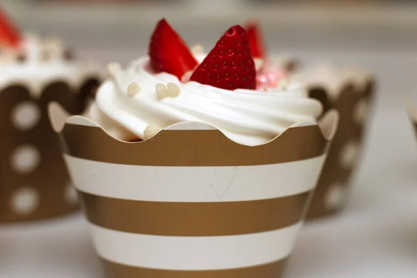 Крупным планом кексы со взбитыми яйцами кремом украшены свежей клубникой и шоколадными шариками на белом фоне. Изолировать — стоковое фото