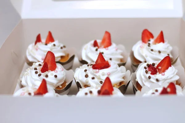 Close-up cupcakes com chantilly ovos creme decorado bolas de morango e chocolate frescos em caixa de papel branco — Fotografia de Stock