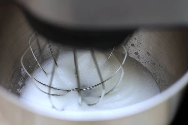 Bir restoranda profesyonel mutfak karıştırıcı yumurta akı kırbaçlama. Yakın çekim çırpılmış beyazlar ve şeker bir metal gezegen karıştırıcı kase.