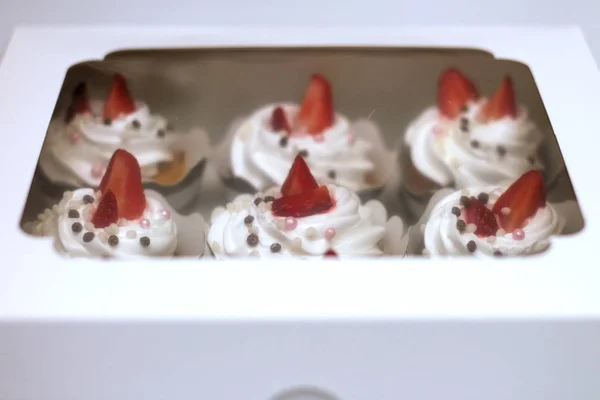 Close-up cupcakes com chantilly ovos creme decorado bolas de morango e chocolate frescos em caixa de papel branco com tampa transparente — Fotografia de Stock