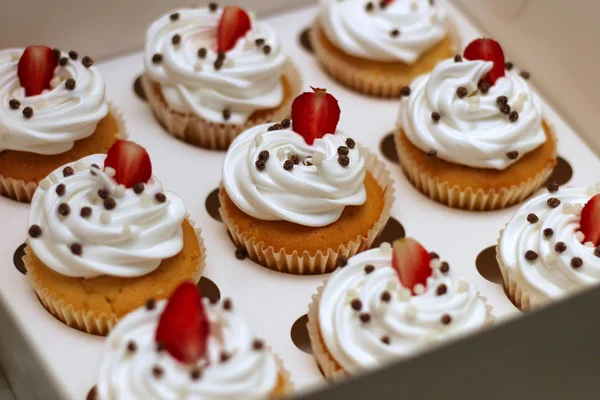 Cupcakes de primer plano con crema de huevos batidos decorados con fresas frescas y bolas de chocolate en caja de papel blanco —  Fotos de Stock