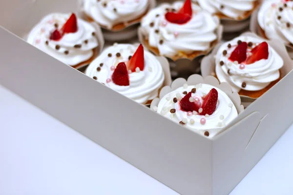 Close-up cupcakes com chantilly ovos creme decorado bolas de morango e chocolate frescos em caixa de papel branco — Fotografia de Stock