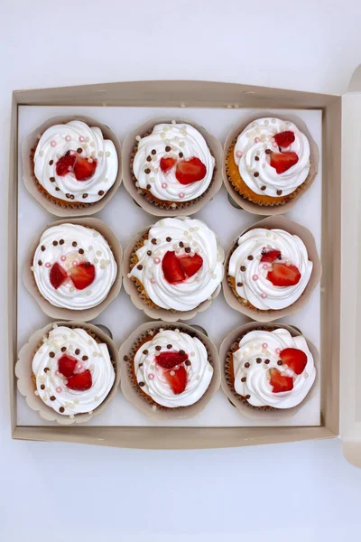 Close-up cupcakes com chantilly ovos creme decorado bolas de morango e chocolate frescos em caixa de papel branco — Fotografia de Stock