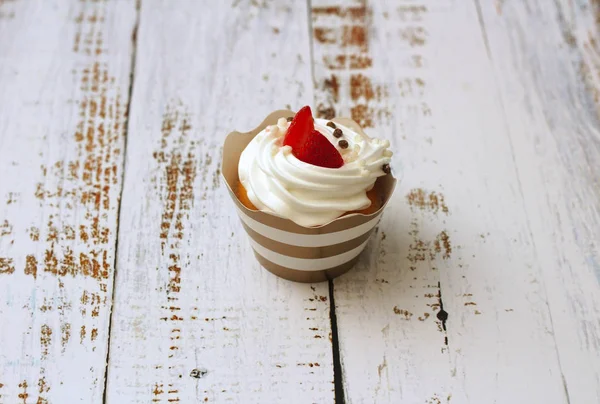 Gros plan cupcake aux œufs fouettés crème décorée de fraises fraîches et de boules de chocolat sur un vieux fond de table en bois blanc . — Photo