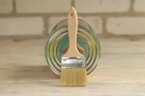 Bir boya fırçası eski bir beyaz vintage ahşap tahta masa üzerinde bir metal olabilir yatıyor. Arka planda tuğla duvar. Metin veya logo için yer.