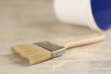 Bir boya fırçası eski bir beyaz vintage ahşap tahta üzerinde mavi kapaklı plastik bir boya kova yanında. Arka planda tuğla duvar. Metin veya logo için yer.