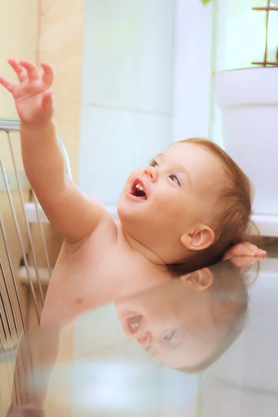 Kleines lächelndes weißes Kind, das auf einem Stuhl am Glastisch in der Küche am Fenster sitzt. das Bild wird vom Tisch reflektiert. — Stockfoto