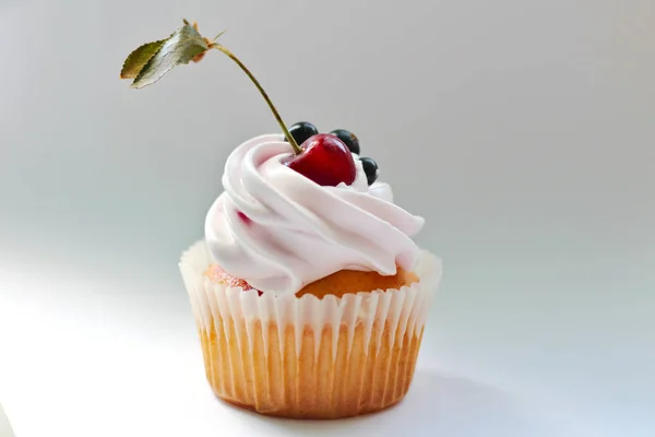 Cupcake isolado com creme, cereja com uma folha e groselha preta em um fundo branco . — Fotografia de Stock