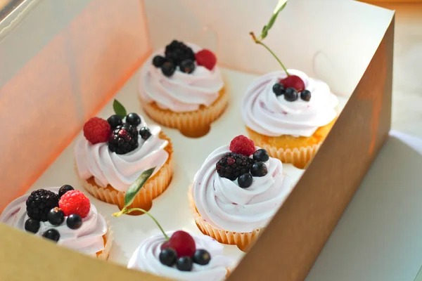 Cupcakes isolados com creme, cereja com uma folha, amora, groselha preta framboesa em uma caixa de artesanato em um fundo branco . — Fotografia de Stock