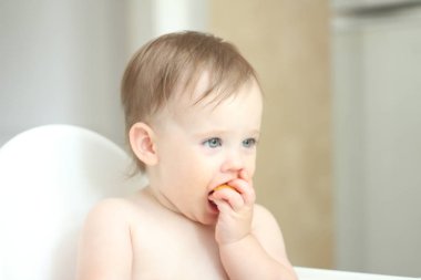 sevimli sarışın çocuk mutfakta bir çocuk sandalyesinde oturur ve sulu bir şeftali sarışın çocuk yemek mutfakta bir çocuk sandalyesinde oturur ve sulu şeftali yemek. Delici bir görünüme sahip küçük kız