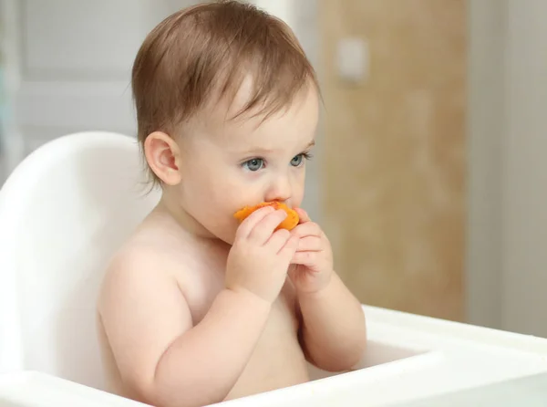 sevimli sarışın çocuk mutfakta bir çocuk sandalyesinde oturur ve sulu bir şeftali yemek. Delici bir görünüme sahip küçük kız