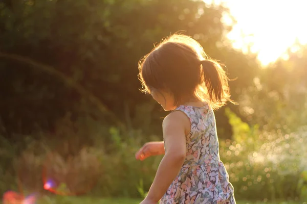 Силуэт маленькой девочки с хвостиком в цветочном платье на открытом воздухе в лучах солнечного заката — стоковое фото