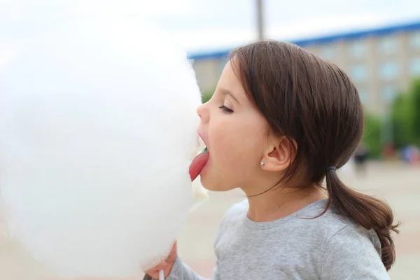 Petite fille avec des nattes essaie de mordre une grosse boule de barbe à papa lors d'une célébration de la ville — Photo