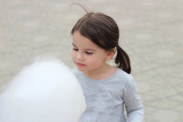Niña con coletas sostiene en su mano una gran bola de algodón de azúcar en una celebración de la ciudad — Foto de Stock