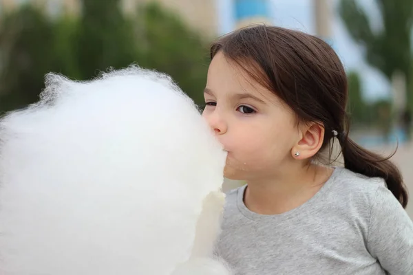 Маленькая девочка с косичками держит в руке большой шар сахарной ваты на городском празднике — стоковое фото
