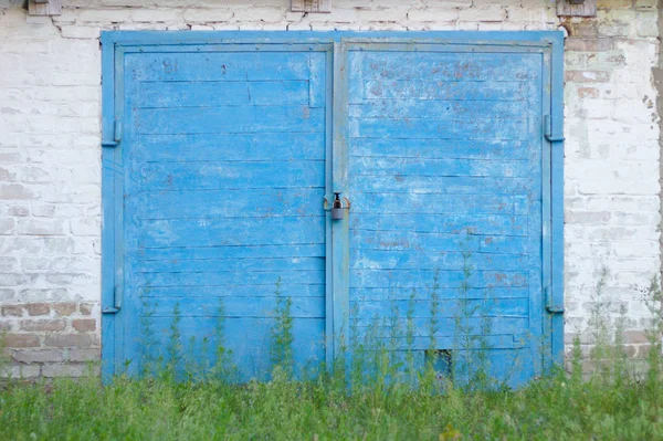 Vieja puerta de madera azul con un candado en una pared de ladrillo. Hierba verde en primer plano —  Fotos de Stock