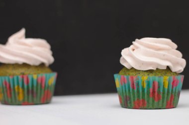 Koyu arkaplanda beyaz bir masada krem şapkalı, çok renkli kağıtlı yeşil kapkekler. Pastaya odaklan, alan etkisinin derinliği