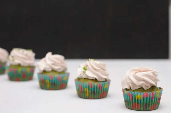 Grüne Cupcakes mit cremefarbenem Hut auf einem weißen Tisch vor dunklem Hintergrund. Fokus auf Kuchen, Tiefenschärfeeffekt — Stockfoto