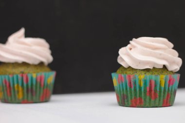 Koyu arkaplanda beyaz bir masada krem şapkalı, çok renkli kağıtlı yeşil kapkekler. Pastaya odaklan, alan etkisinin derinliği