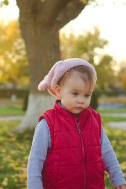 Pembe şapkalı ve kırmızı yelekli küçük bir çocuk sonbahar parkında koşuyor. Güzel sonbahar açık havada güneşli bir gün.