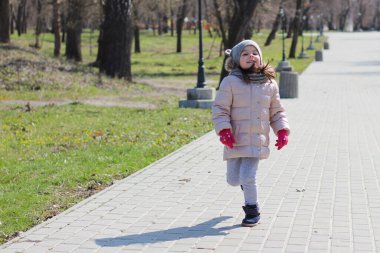 Sıcak giyimli, eldivenli küçük kız parkta koşuyor.