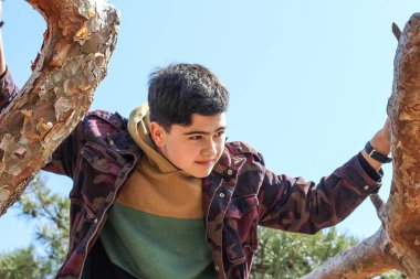 Mavi gökyüzüne karşı ağaçta el ele tutuşan genç bir çocuğun portresi