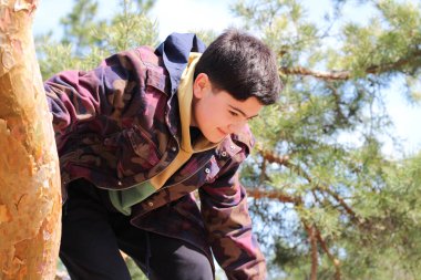 Beyaz çocuk mavi gökyüzüne karşı bir ağaç gövdesine tırmanıyor. Açık havada spor aktiviteleri