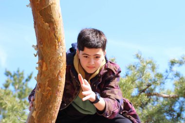 Haki ceketli bir çocuk ağaç gövdesine tırmanıyor. Açık hava aktivitesi