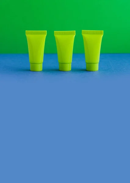 3 three blank green cosmetic tubes on blue background. Simple plastic containers, mock up packaging design. shallow depth of field, copy space photography.