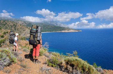 Erkek bir sırt çantası ile Akdeniz kıyısında duruyor ve mesafe içine görünüyor