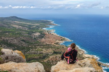 Kayalıklarda oturan ve Akdeniz 'e bakan bebekli bir anne.