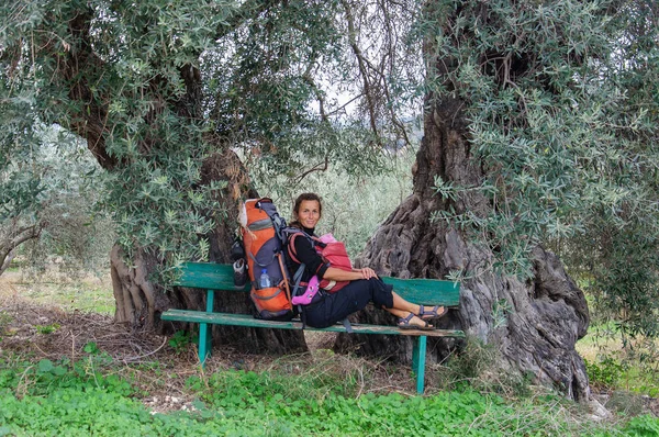 Mom and baby sit on bench under two old olive trees — Stock Photo, Image