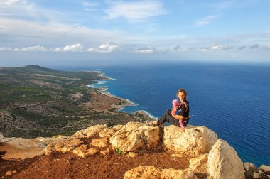 Kayalıklarda oturan ve Akdeniz 'e bakan bebekli bir anne.