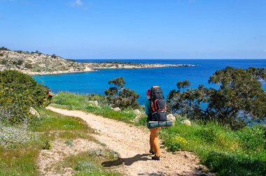 çiçekler deniz boyunca arasında yol boyunca yürüyüş sırt çantası ile şapkalı şık kız